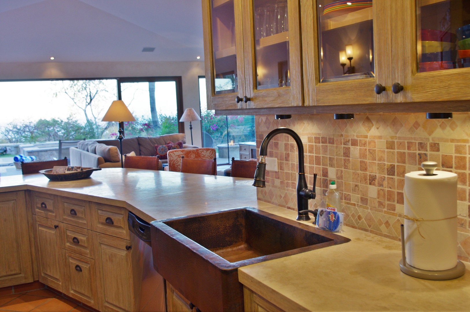 Your vacation kitchen features warm wood cabinets, elegant tile backsplash, and a distinctive copper farmhouse sink—perfect for preparing meals while enjoying serene views of the outdoor landscape beyond.