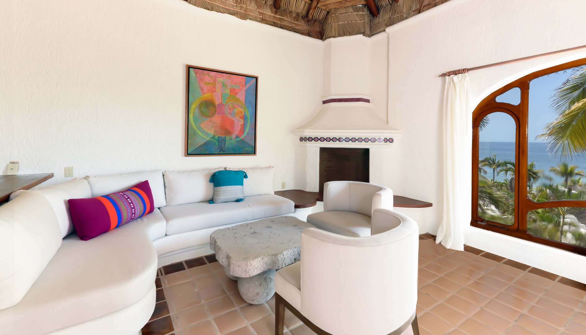You'll love sinking into this bright, open living space with its unique architectural touches—colorful art, cozy fireplace, and stunning ocean views through the arched window.