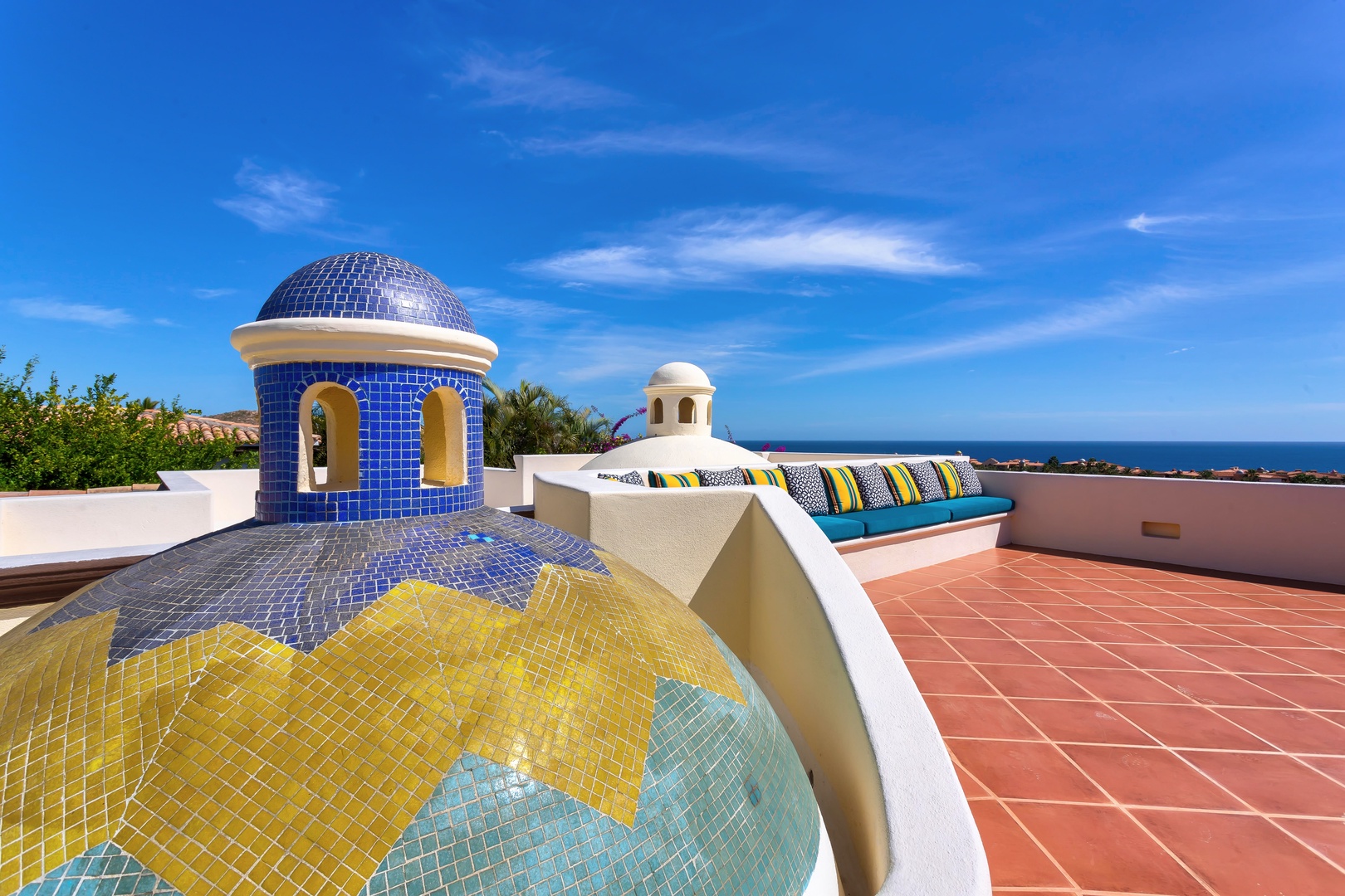 Stunning rooftop terrace with colorful mosaic dome, cushioned seating, and panoramic ocean views under brilliant blue skies.