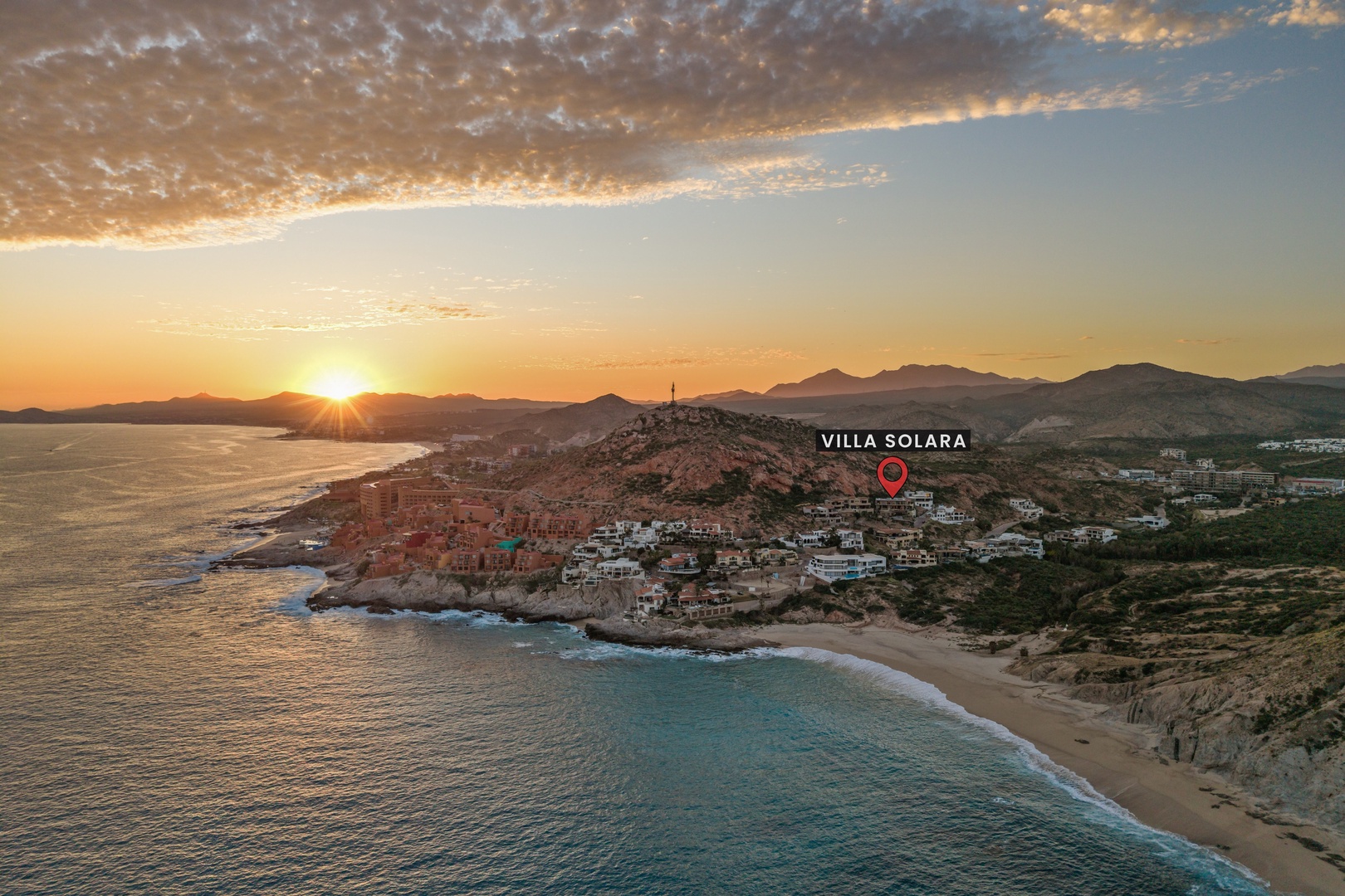 Aerial view of Villa Solara's coastal location at sunset, showcasing the scenic beachfront community and dramatic mountain backdrop of the surrounding area.