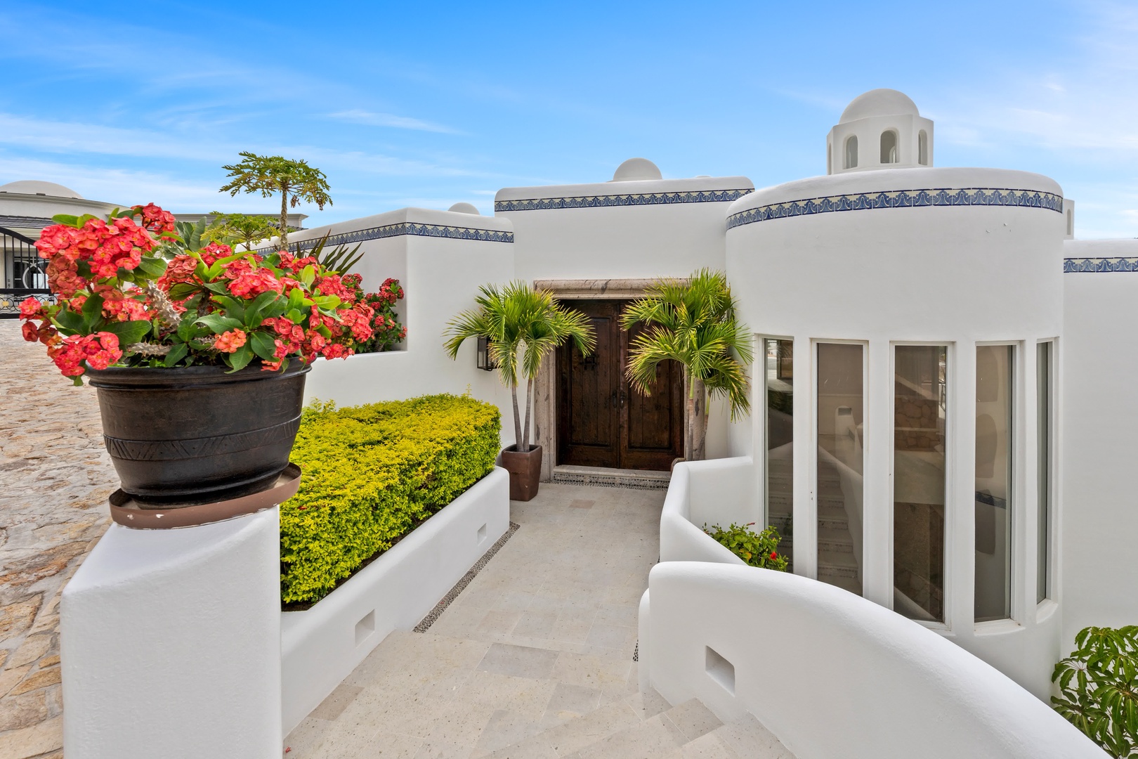 Stunning white villa entrance with vibrant coral flowers and tropical palms creating an elegant Mediterranean-style welcome.