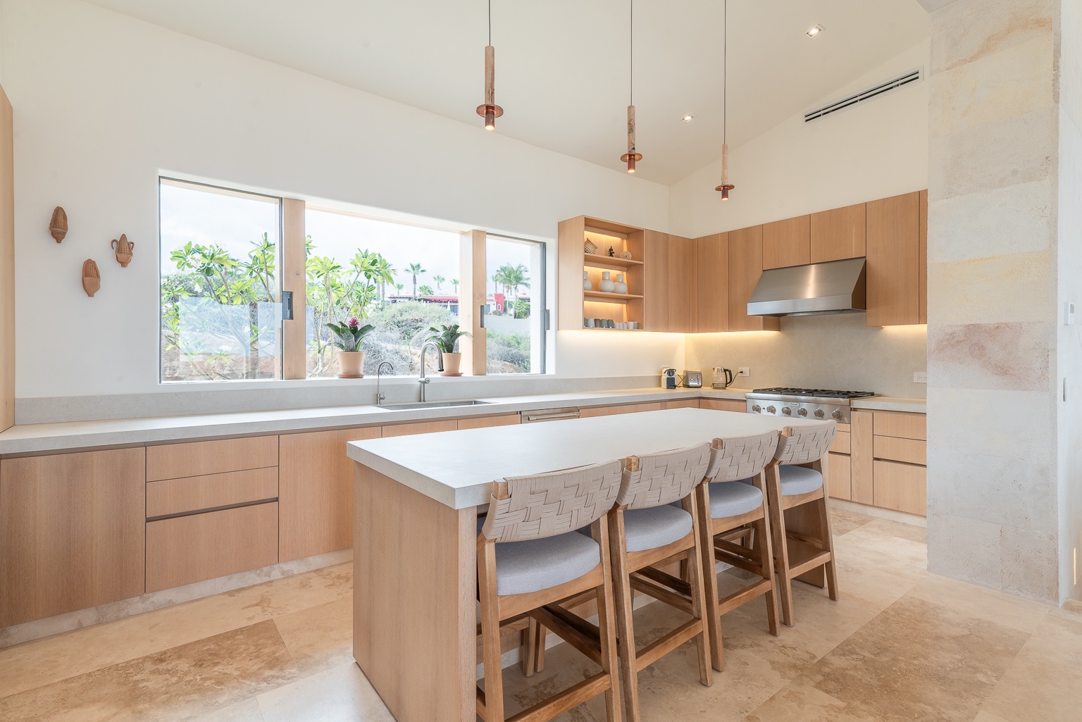 Picture yourself preparing meals in this bright, modern kitchen with its sleek island seating, warm wood cabinetry, and sunny garden views flowing through expansive windows.