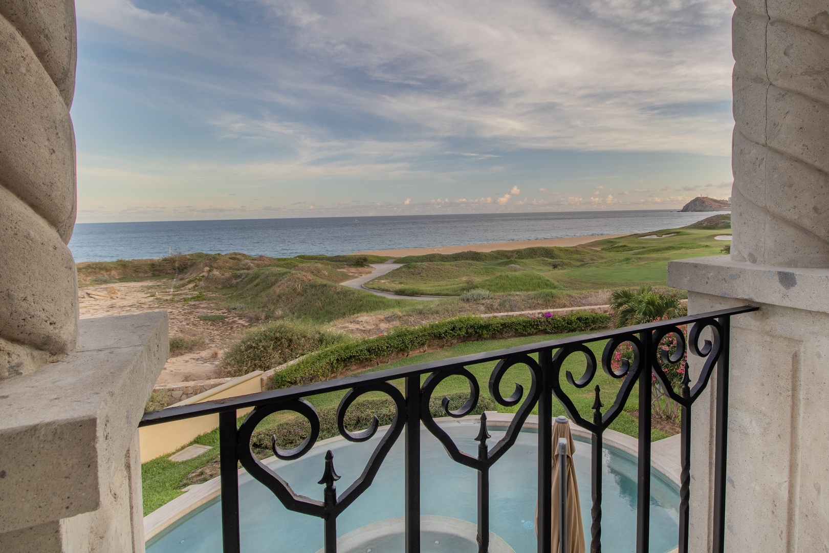 Panoramic coastal scenery with ocean, rolling dunes, and manicured golf greens framing the property's entrance columns and pool area below.