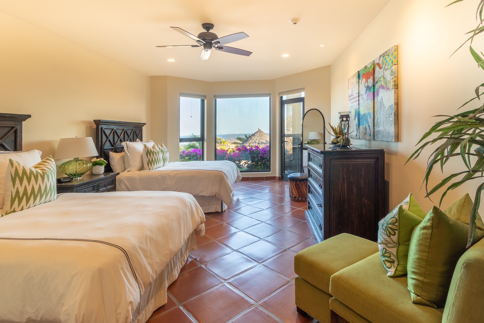 Unwind in your spacious bedroom with two comfortable beds, a cozy seating area, and views of vibrant flowers and beachside palapa just beyond your door.