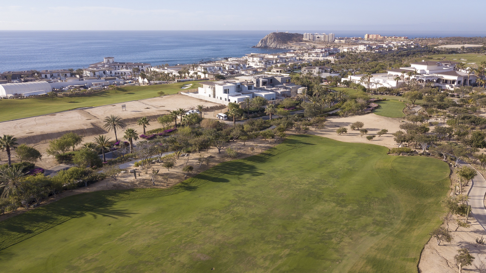Aerial view showcasing the pristine coastal golf course with lush fairways, nearby residential areas, and stunning ocean backdrop.