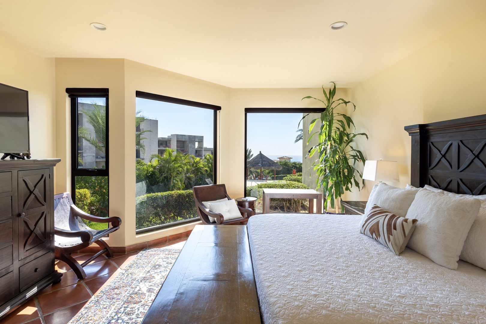 Unwind in your elegant bedroom with panoramic windows framing lush tropical gardens and distant mountains.