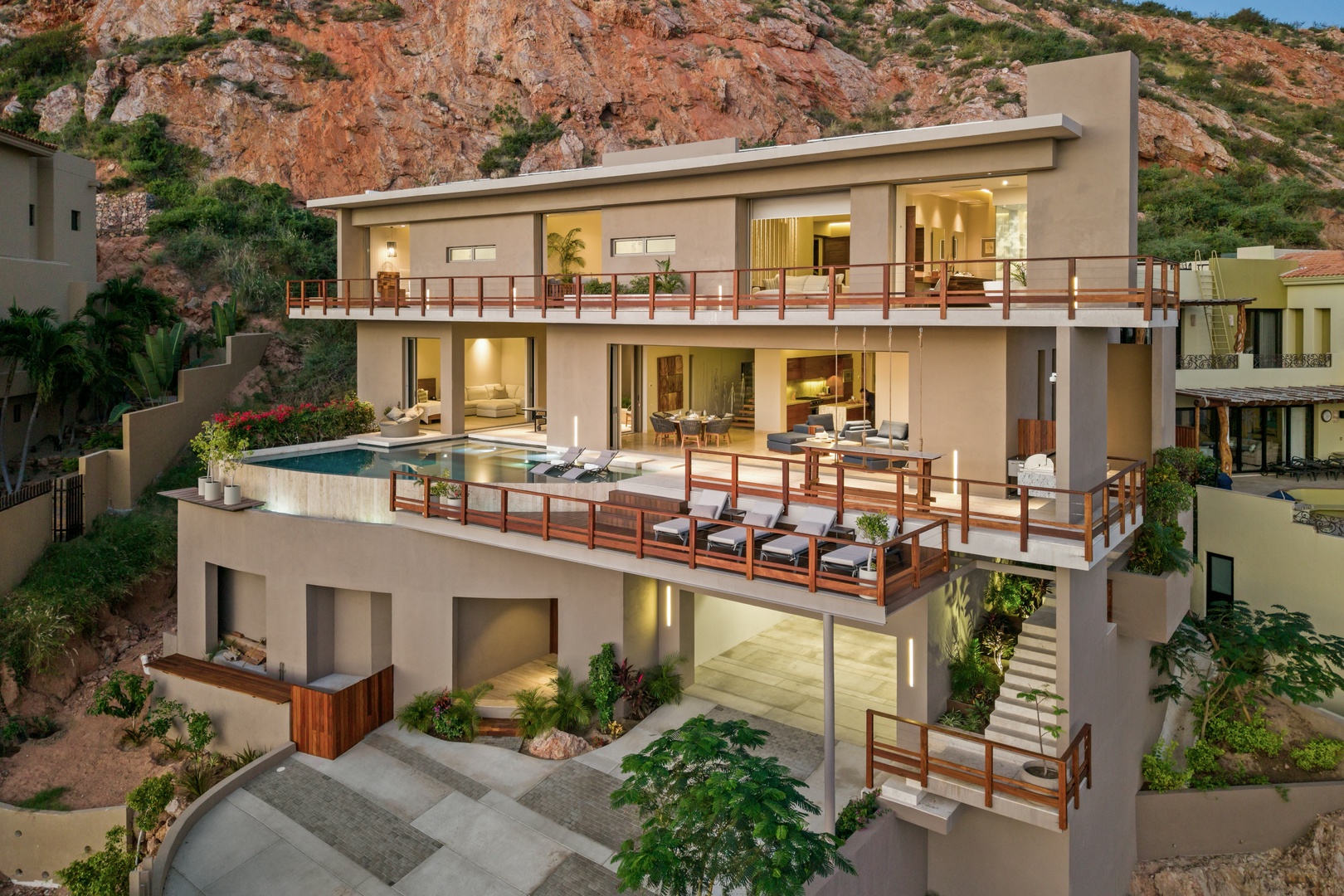 Modern terraced villa nestled into rugged hillside, featuring multiple outdoor lounging decks, a sparkling pool, and tropical landscaping against a dramatic mountain backdrop.