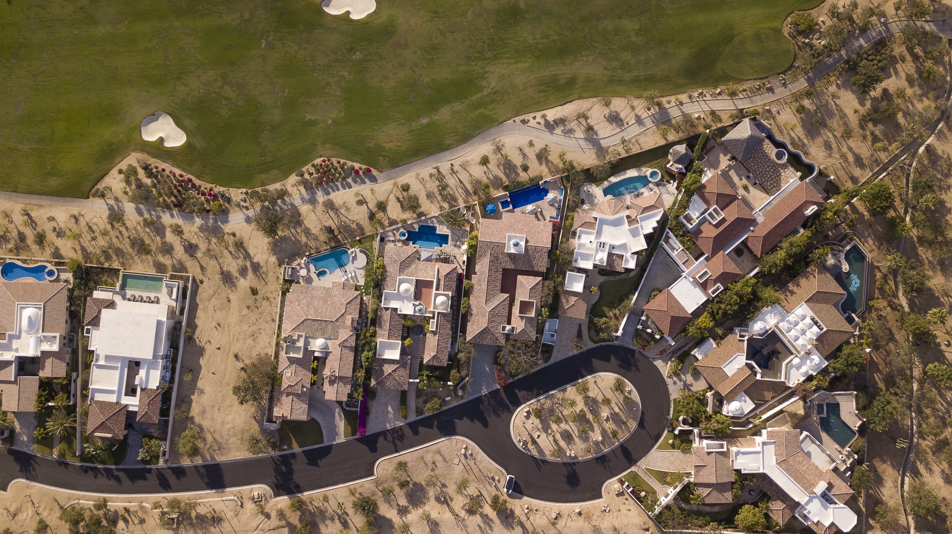 Aerial view of an exclusive residential community featuring luxury homes with private pools nestled in a scenic desert landscape setting.