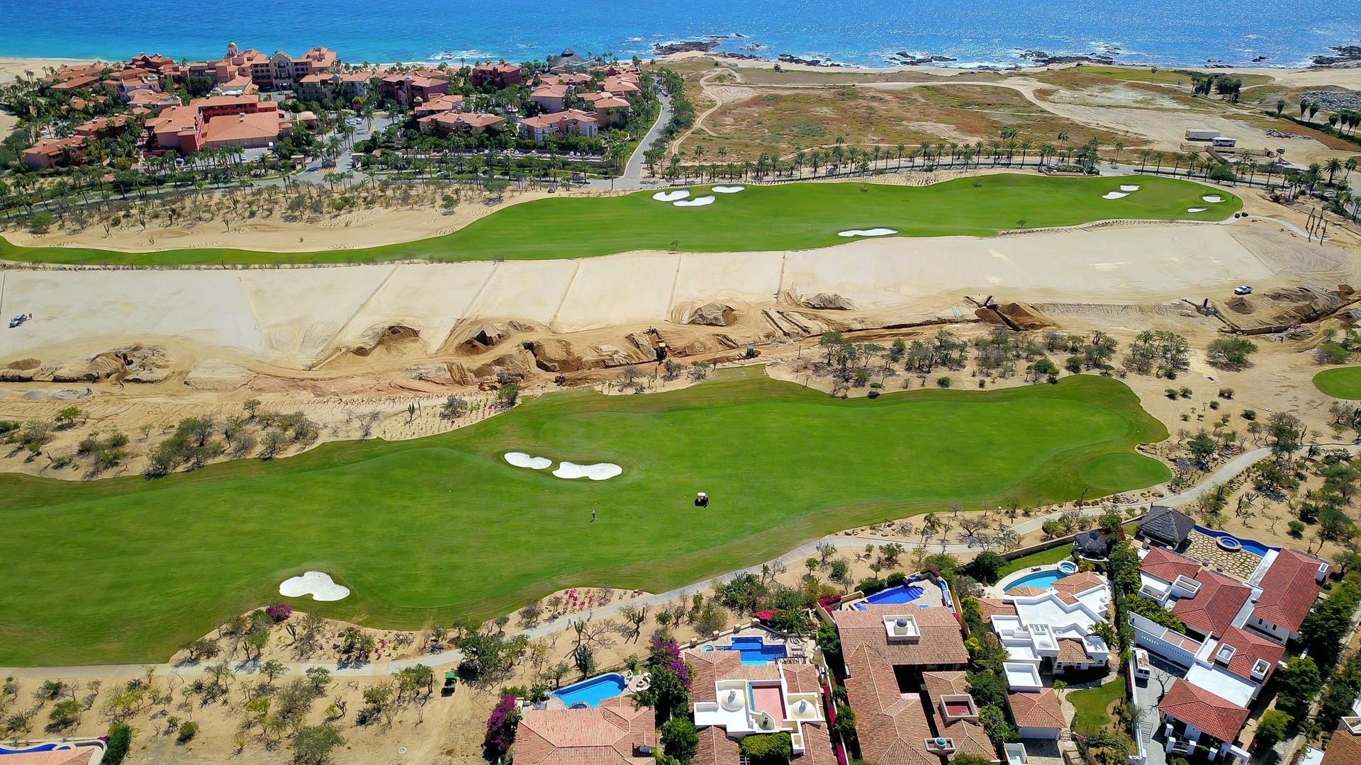 Aerial view showcases championship golf course fairways stretching toward pristine coastline, with resort villas and Mediterranean architecture dotting the landscape.