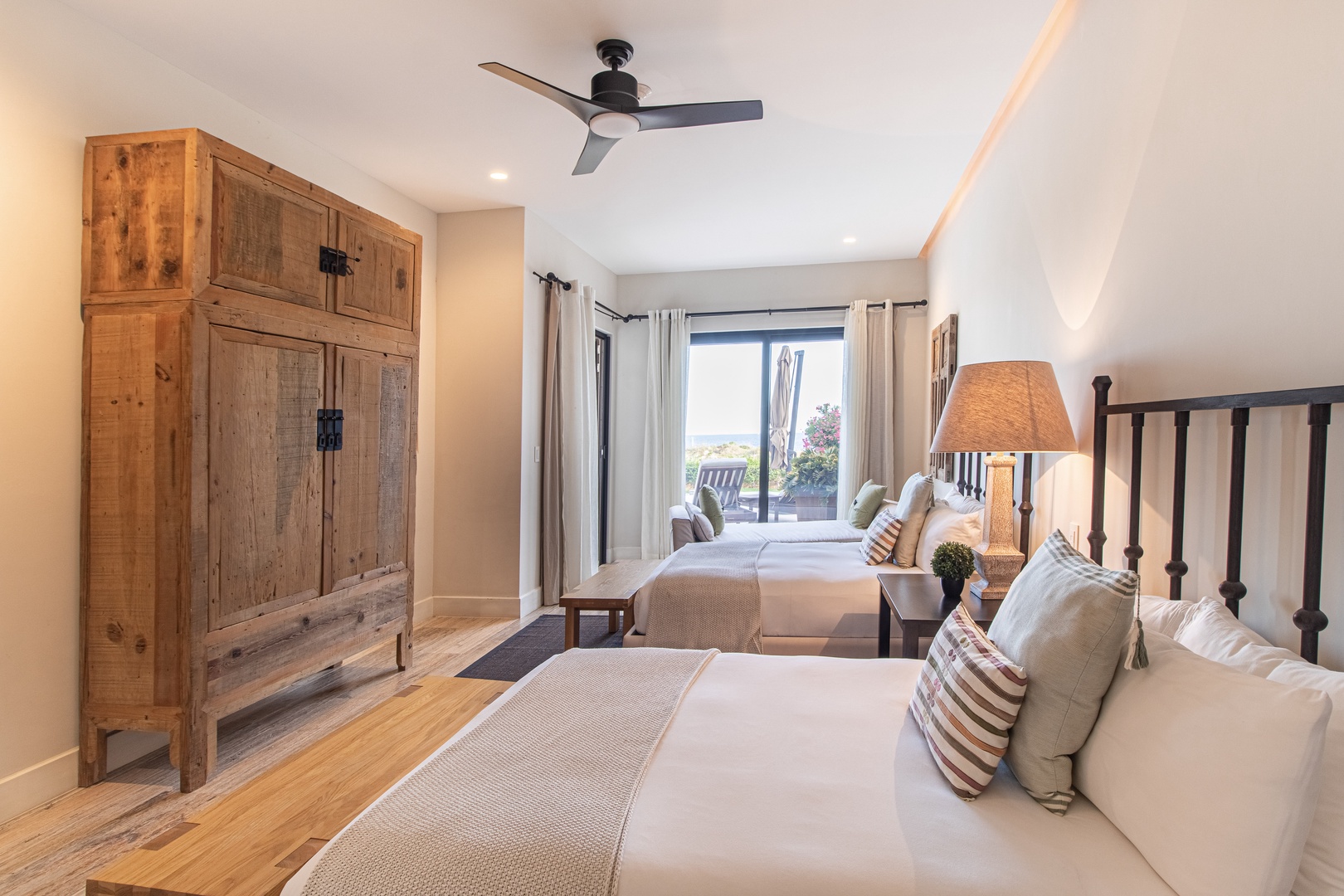 Your peaceful bedroom retreat features twin beds with crisp linens and charming striped accents. Natural light streams in through French doors, while a ceiling fan keeps you comfortable.