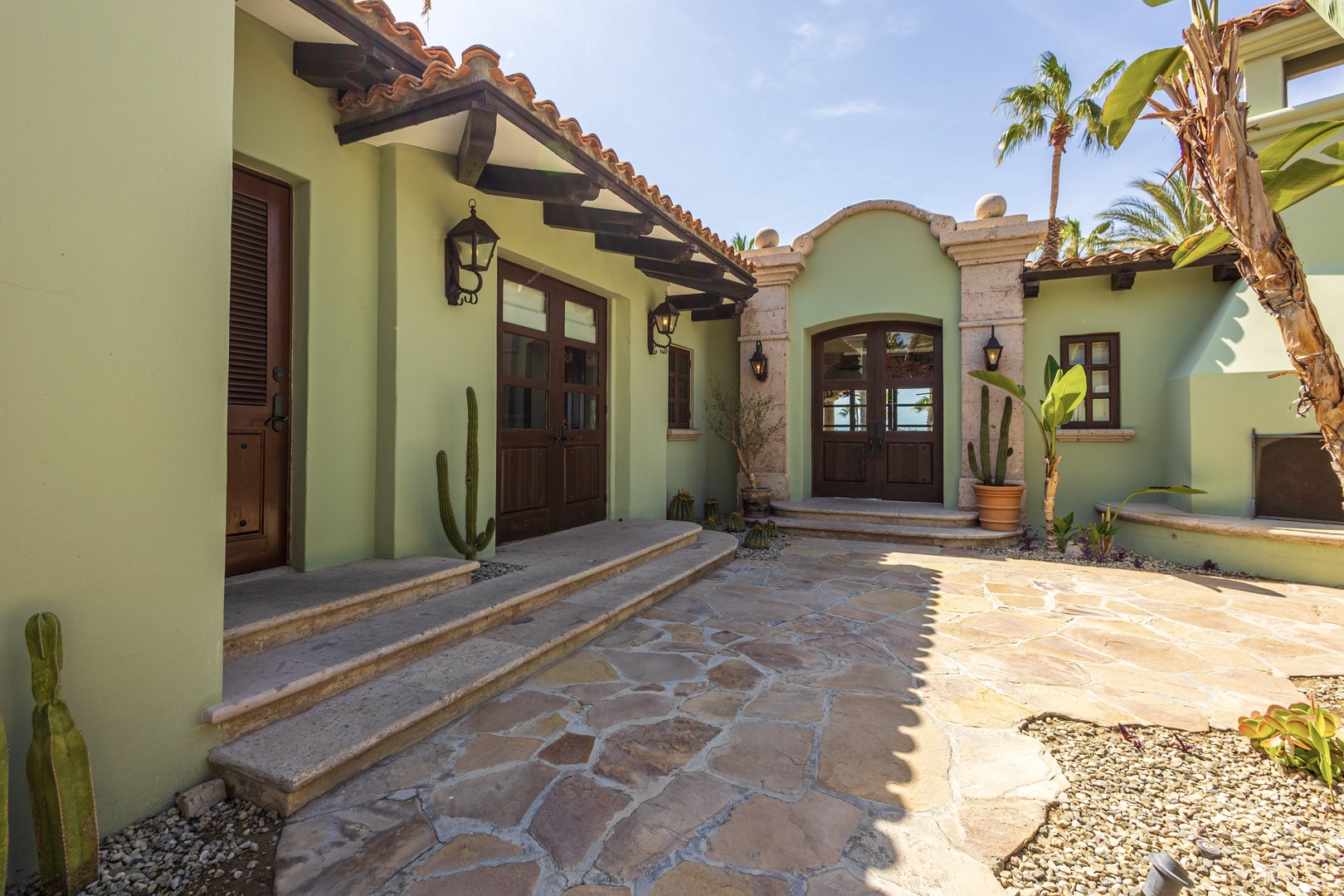 Beautiful Spanish colonial architecture welcomes guests with traditional tile roofing, natural stone courtyard, and tropical landscaping creating an authentic desert oasis entrance.