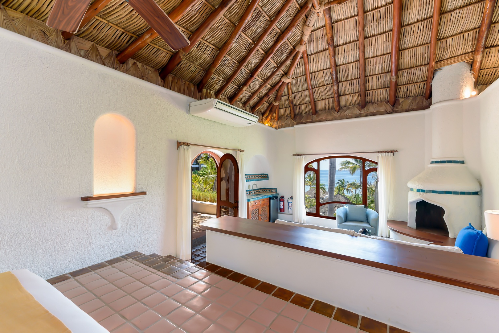 You'll love the authentic palapa thatched ceiling and bright white walls that frame stunning ocean views through arched windows, blending tropical charm with modern comfort in your private retreat.