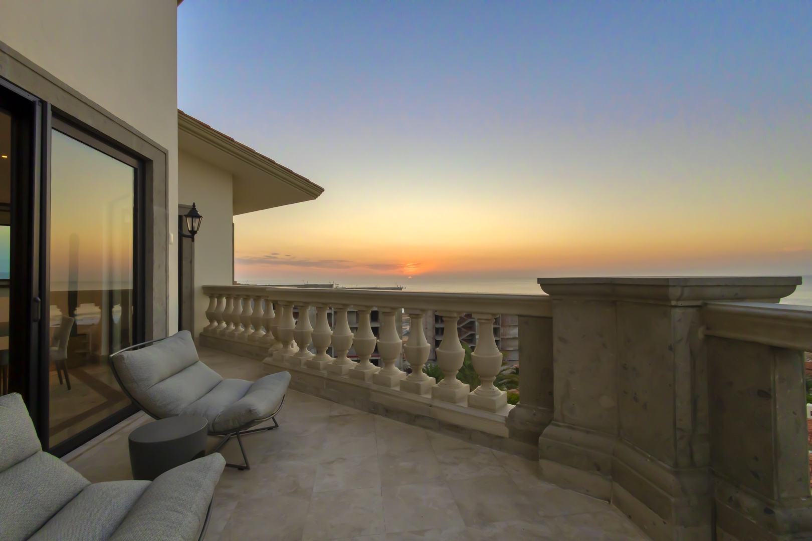 A private balcony with elegant stone balustrade frames coastal sunsets—ideal for morning coffee or evening reflection with panoramic ocean views at your doorstep.