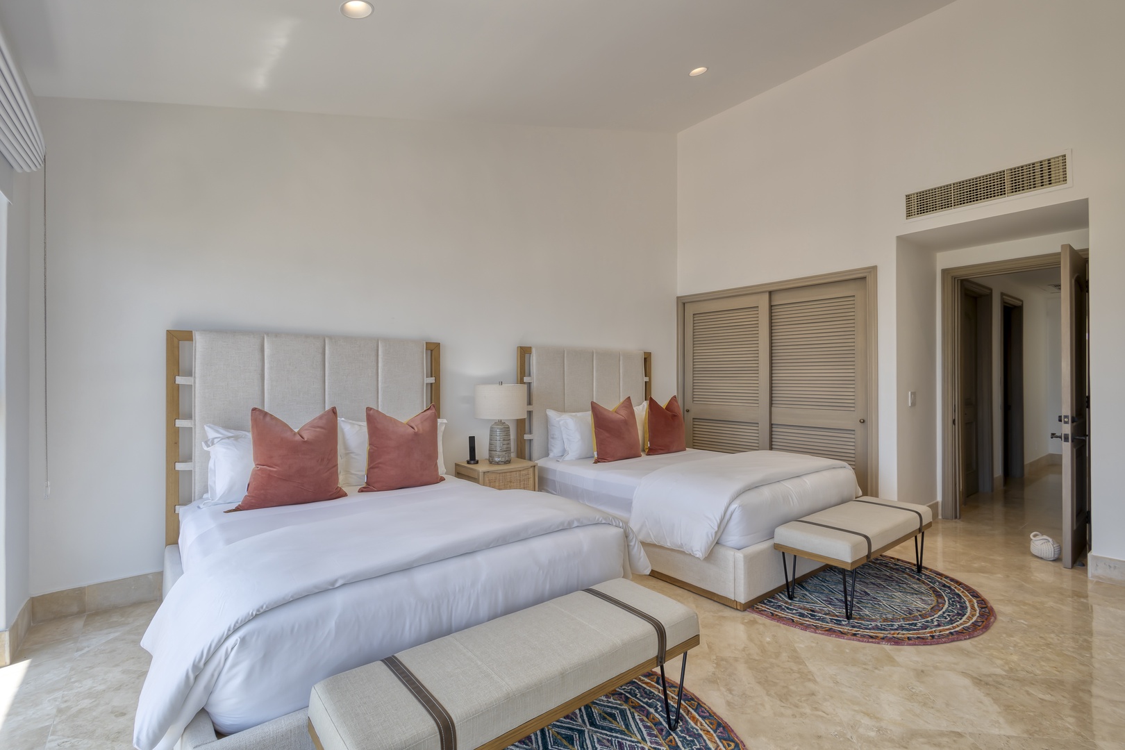 Sink into plush bedding in this serene guest room, where two luxurious beds await your perfect night's sleep. Soft coral pillows add warmth, while elegant benches and vibrant rugs invite you to relax in style.