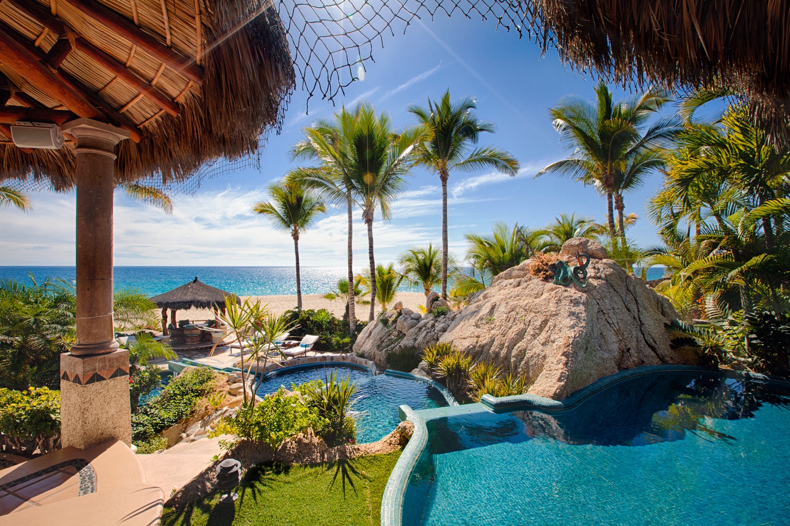 Tropical paradise with stunning pool oasis featuring natural rock formations and direct beach access through swaying palms.