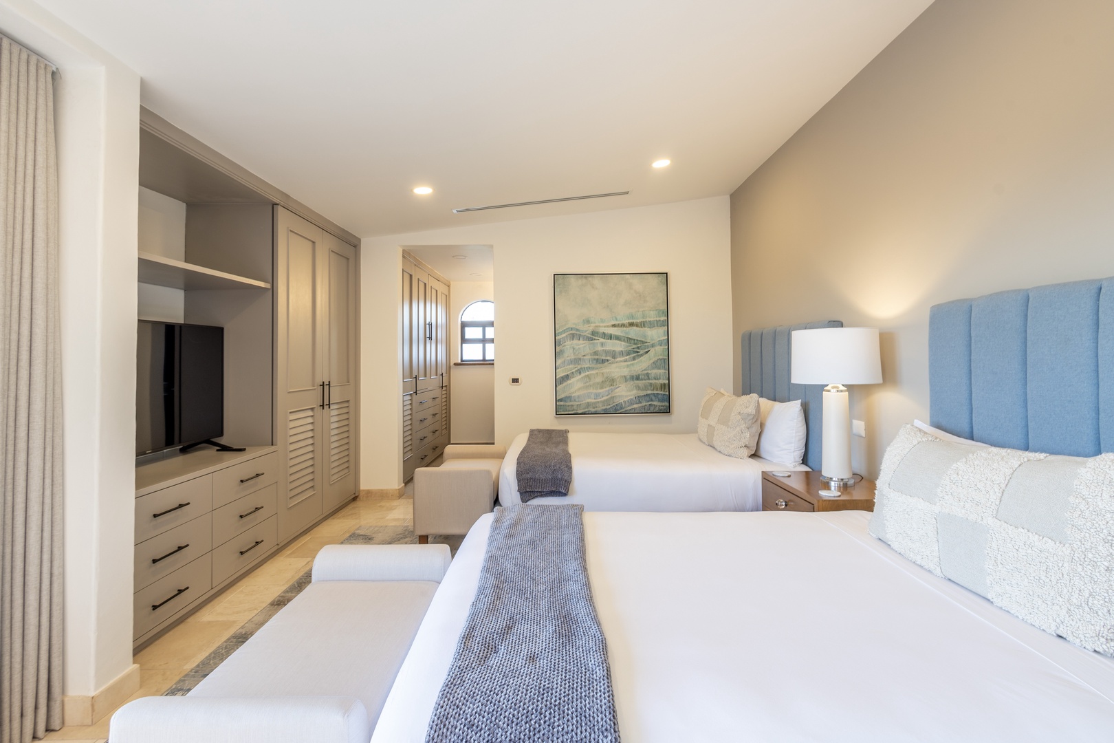 Unwind in your serene bedroom featuring two plush beds with soft linens, a mounted flat-screen TV, ample wardrobe space, and calming coastal artwork that invites restful nights.