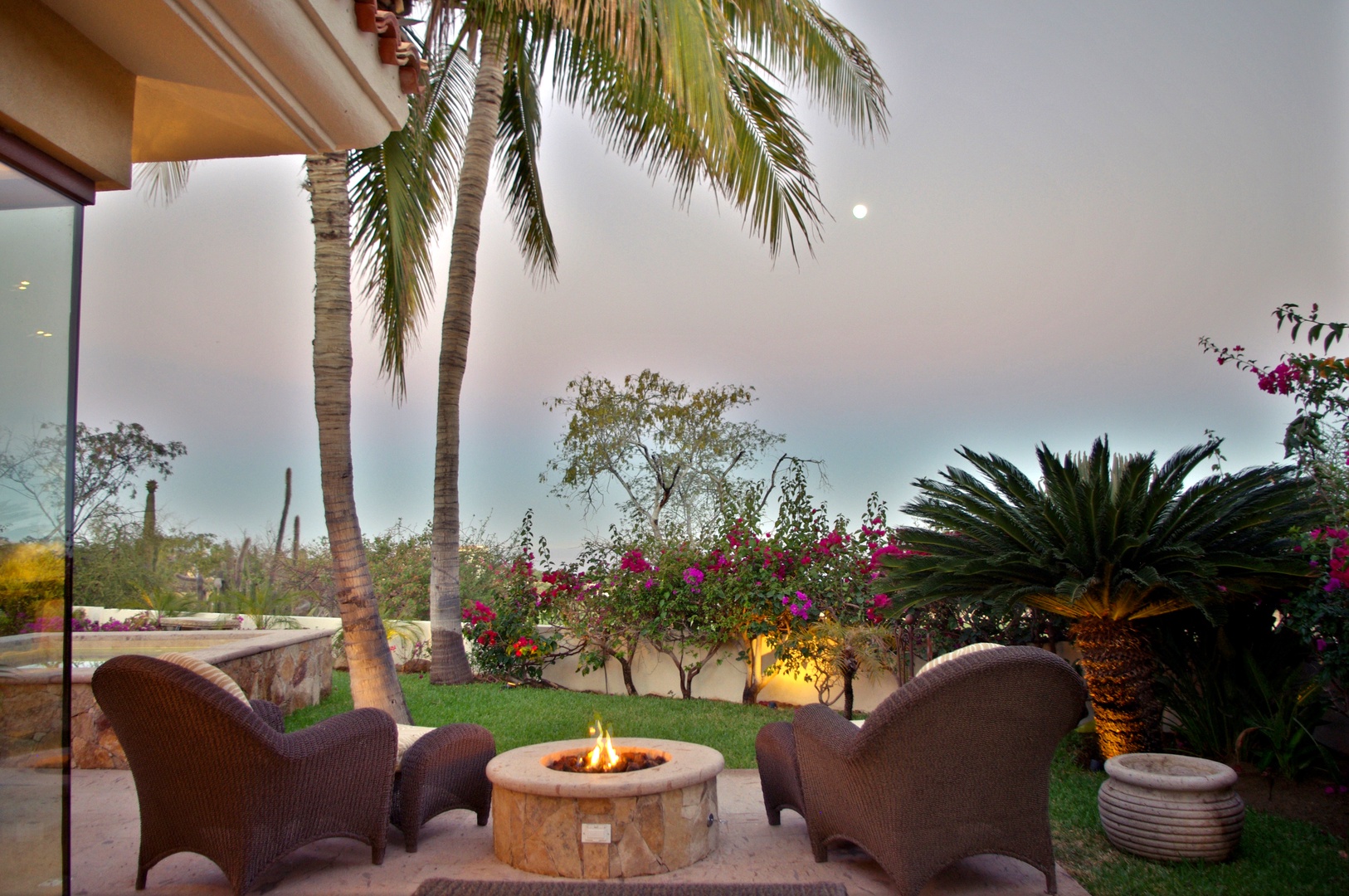 Unwind by the fire pit in your private courtyard, surrounded by lush palms, vibrant blooms, and serene desert skies—your peaceful escape awaits.