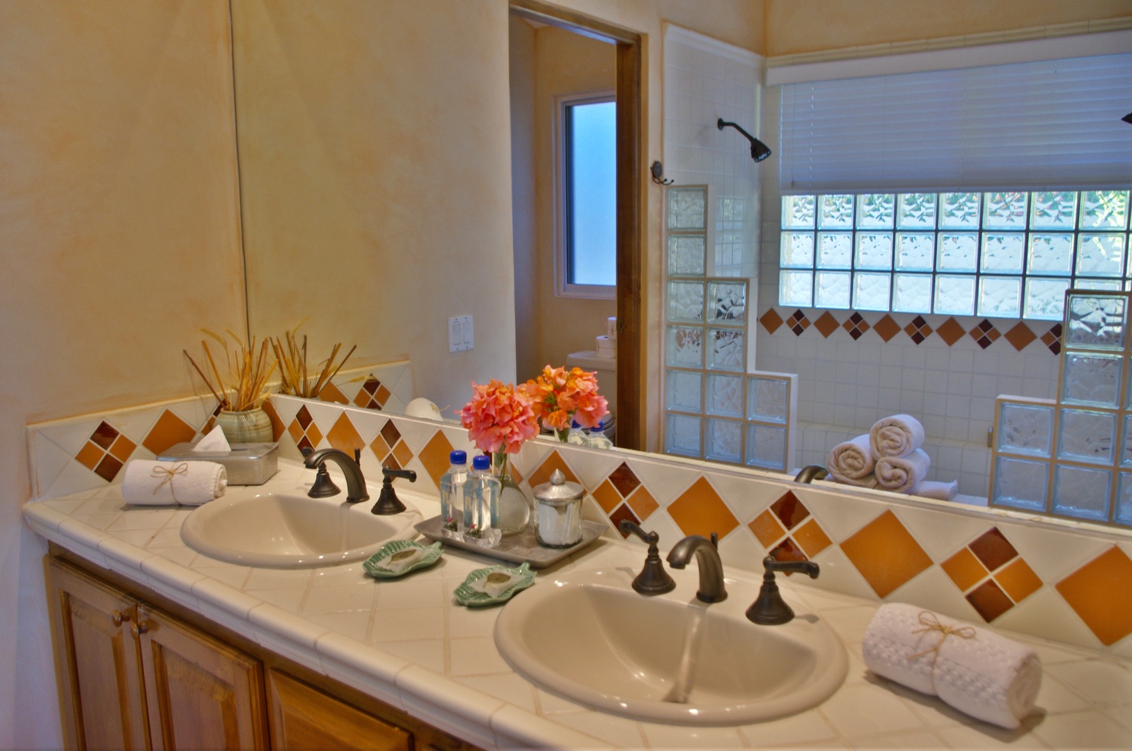 Step into your private bathroom where dual sinks with Mediterranean-inspired tilework and fresh towels await, while glass-block windows fill the space with natural light.