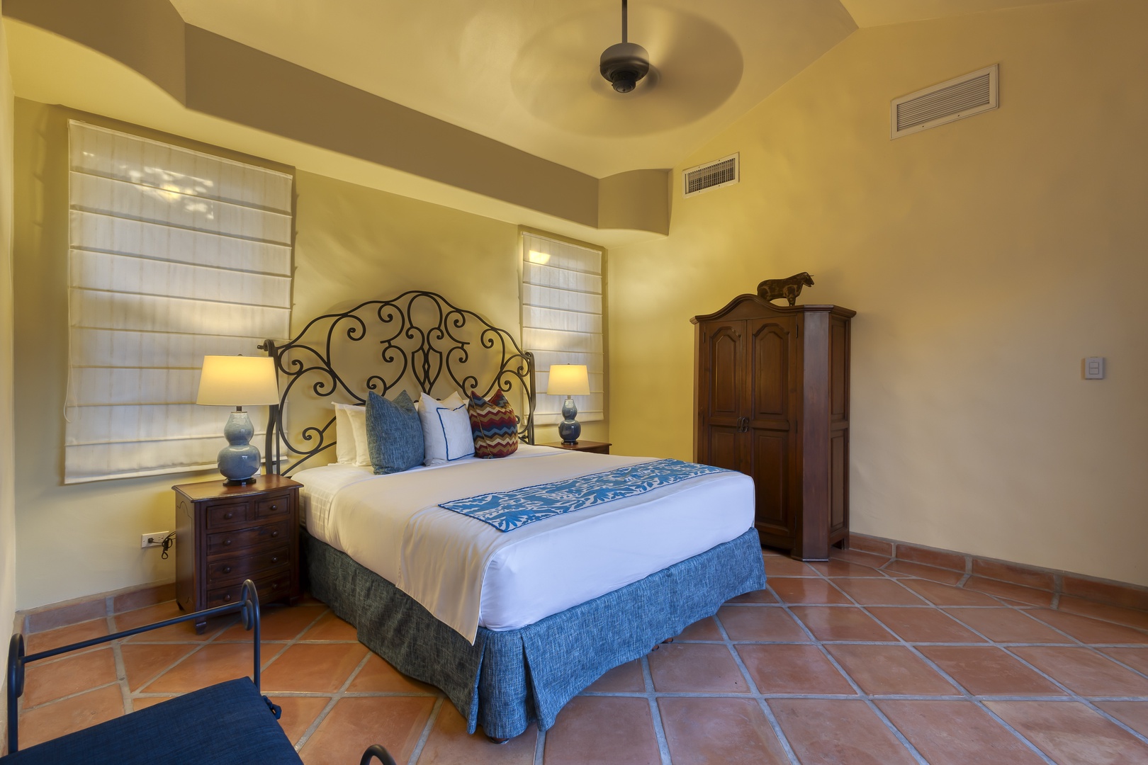 Unwind in your elegant bedroom featuring handcrafted ironwork, warm terracotta floors, and soothing blue accents that invite peaceful rest.
