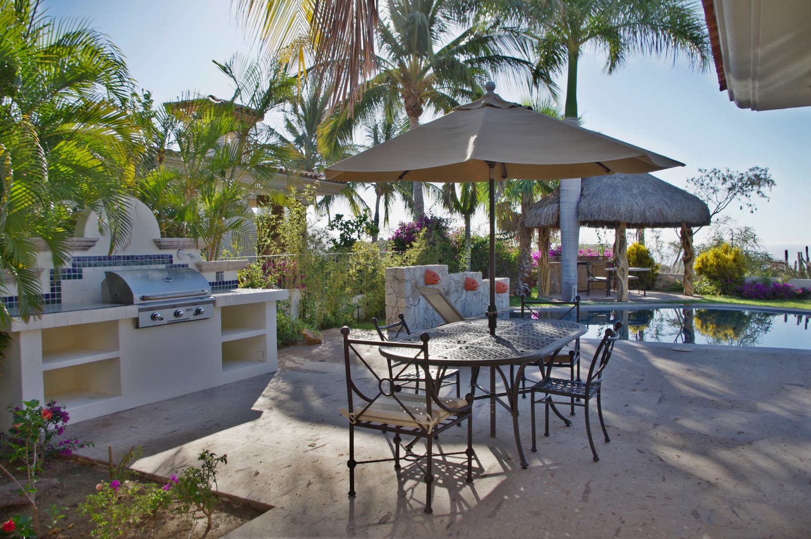Your private outdoor oasis awaits—gather around the shaded dining table, grill up a feast at the built-in BBQ station, then unwind by the sparkling pool surrounded by tropical palms and vibrant blooms.