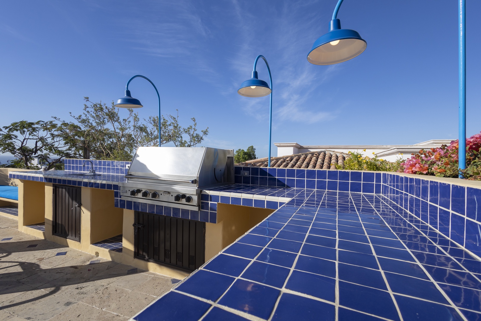 Your rooftop BBQ oasis awaits with stylish blue pendant lighting and vibrant tile counters perfect for outdoor entertaining.
