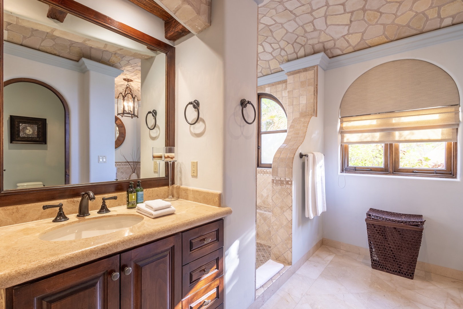 Step into your private retreat with travertine details, elegant wood cabinetry, and a spacious walk-in shower. Natural light pours through arched windows, creating a warm, inviting atmosphere perfect for unwinding after your day.