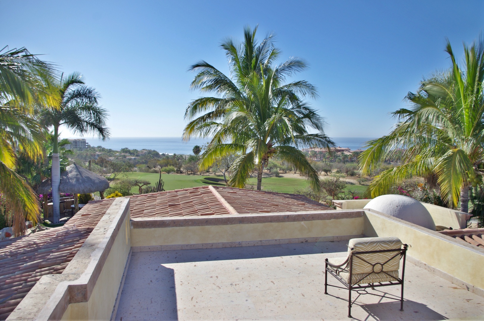 Rooftop terrace with sweeping views of lush golf course fairways, swaying palm trees, and distant ocean vistas framed by coastal hills.
