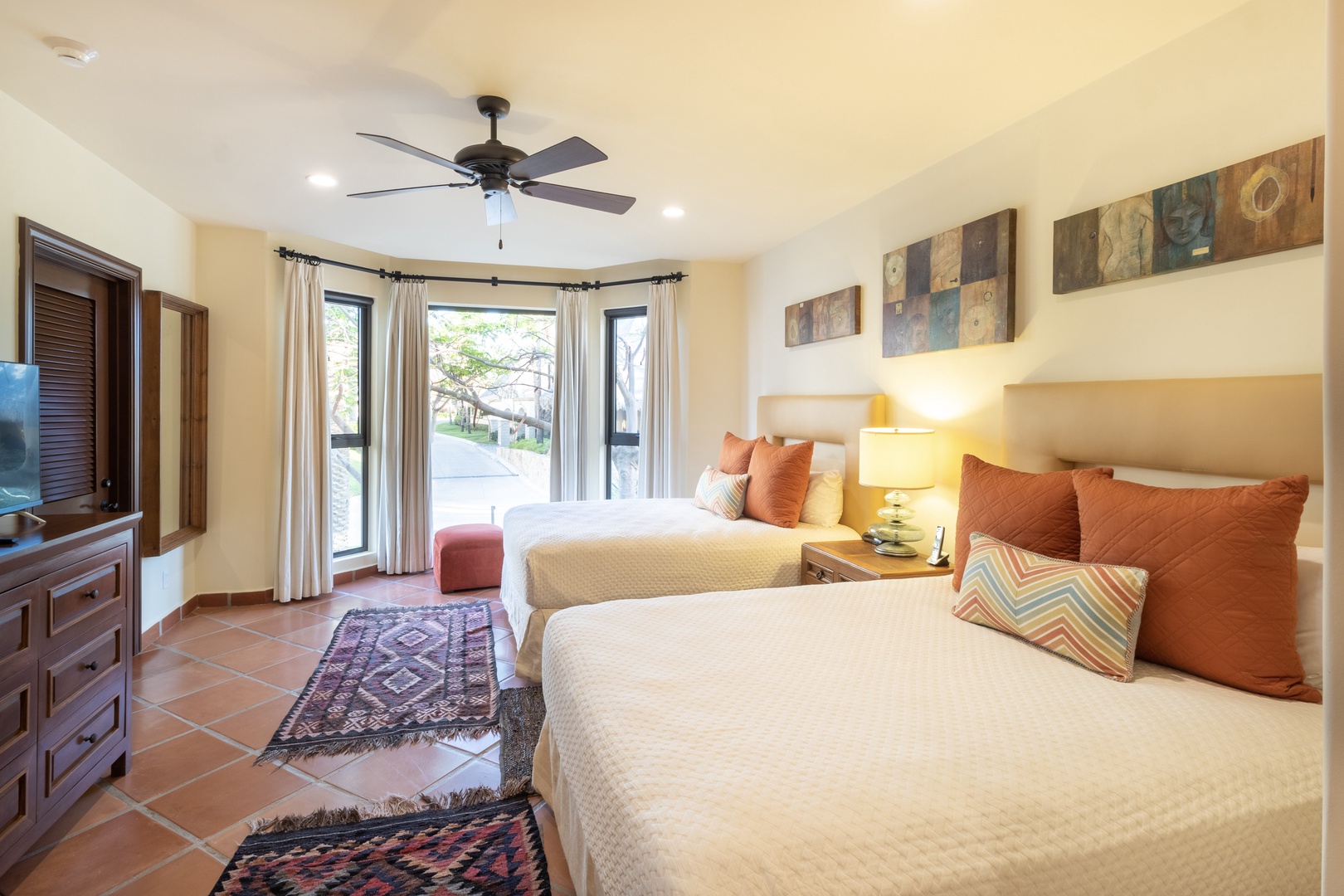 Sink into plush bedding and wake to natural light streaming through bay windows. Your private retreat features two cozy beds, colorful pillows, and a ceiling fan to keep you comfortable.