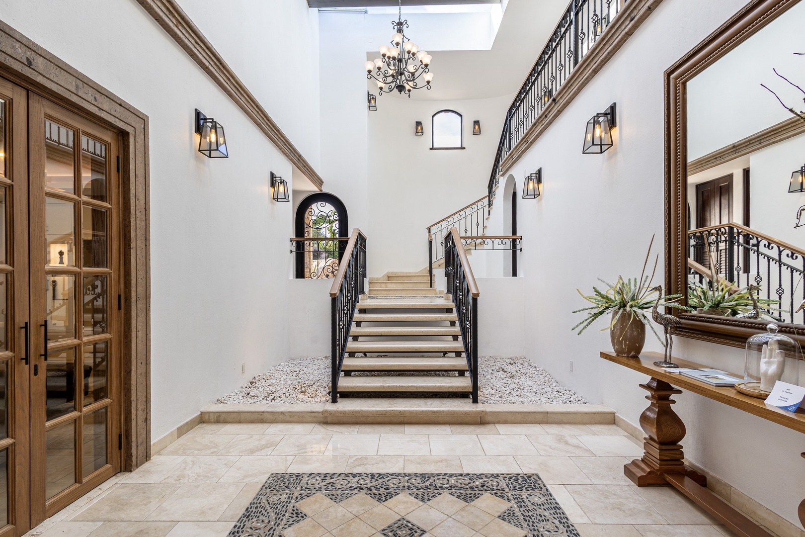 Light pours through the skylight, illuminating elegant wrought-iron railings and a grand staircase that welcomes you into this sophisticated home. Your stay begins in this sun-filled space.