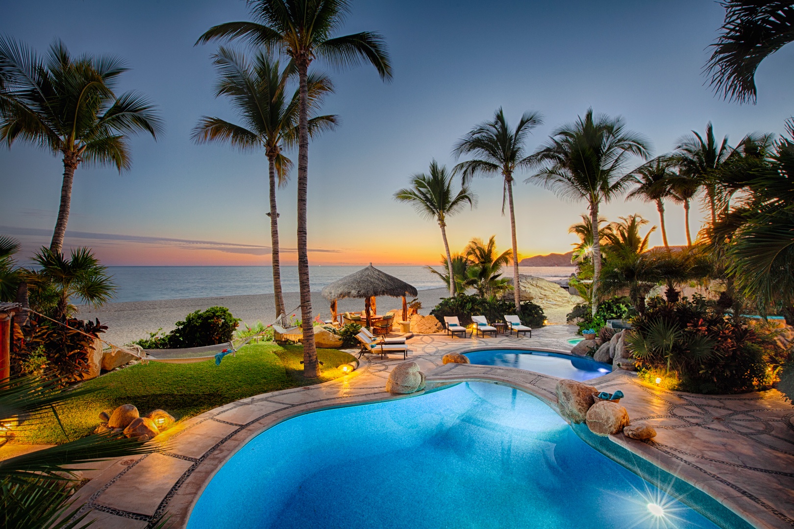 Tropical beachfront paradise with pool, palms, and stunning sunset views creating the perfect backdrop for relaxation.
