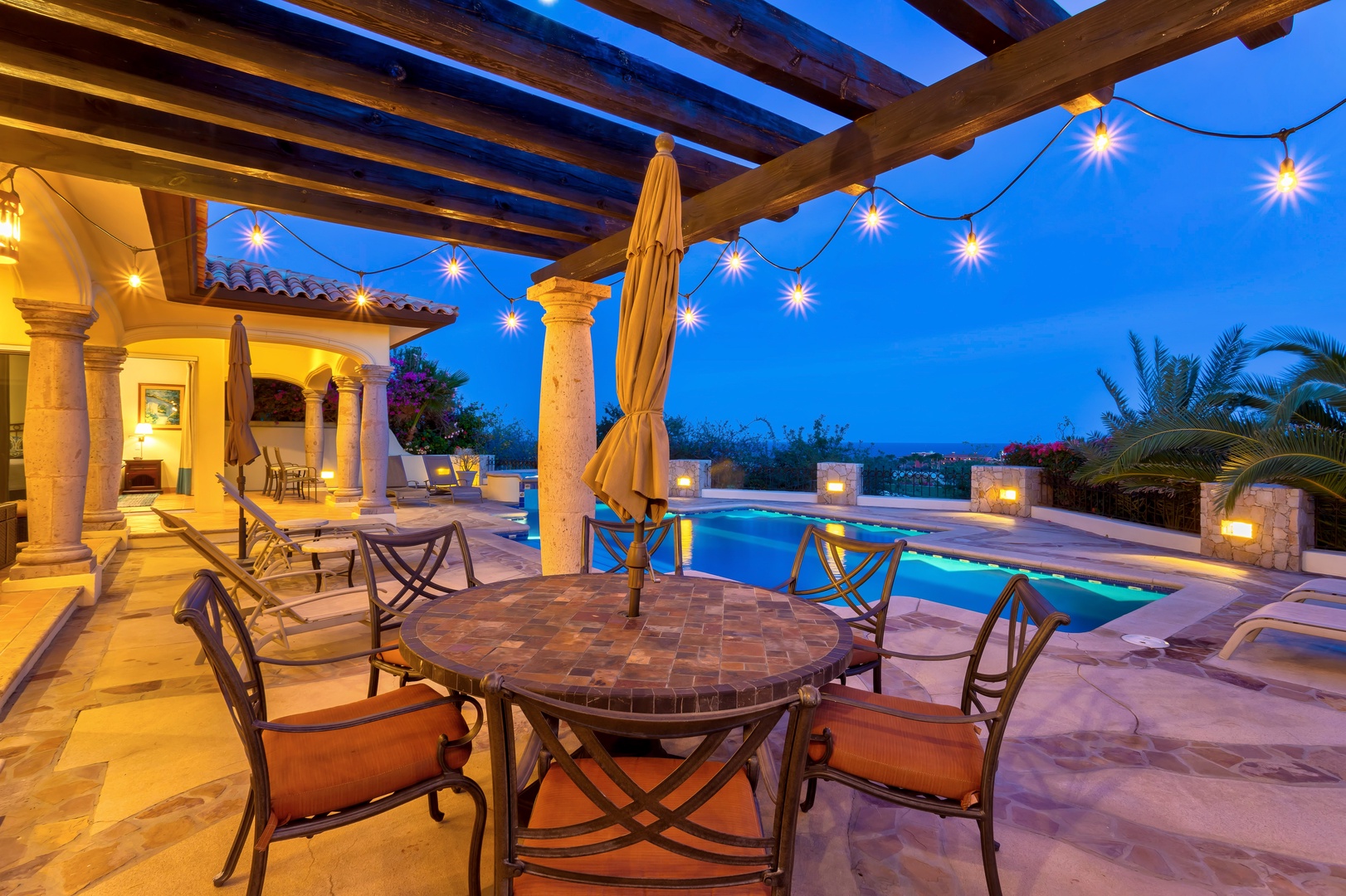 Your covered terrace glows with string lights as twilight settles, creating the perfect ambiance for poolside dining and starlit conversations.