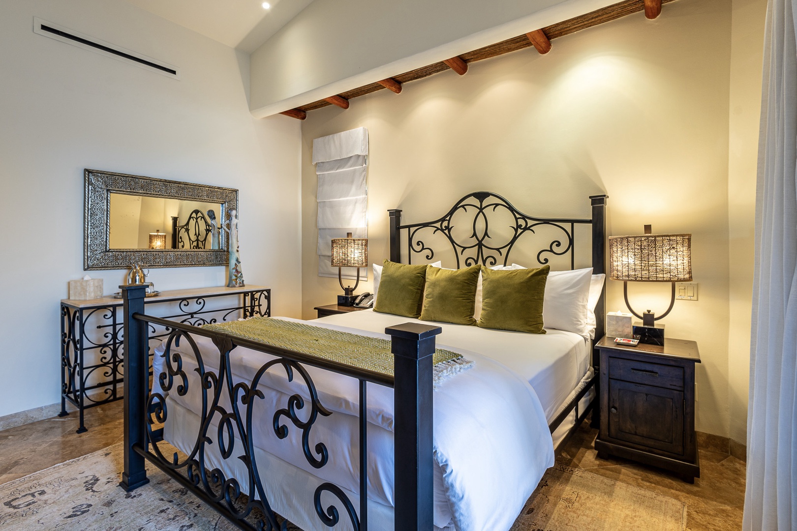 Sink into crisp linens on your plush bed, where elegant ironwork and warm accent pillows welcome you to unwind. Soft lighting and exposed beams create a serene, restful ambiance.