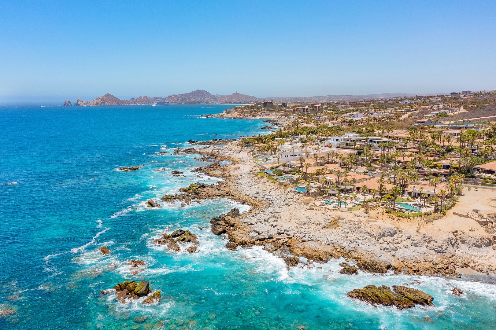 Stunning aerial view of the coastal area with pristine turquoise waters and rocky shoreline stretching toward distant mountains.