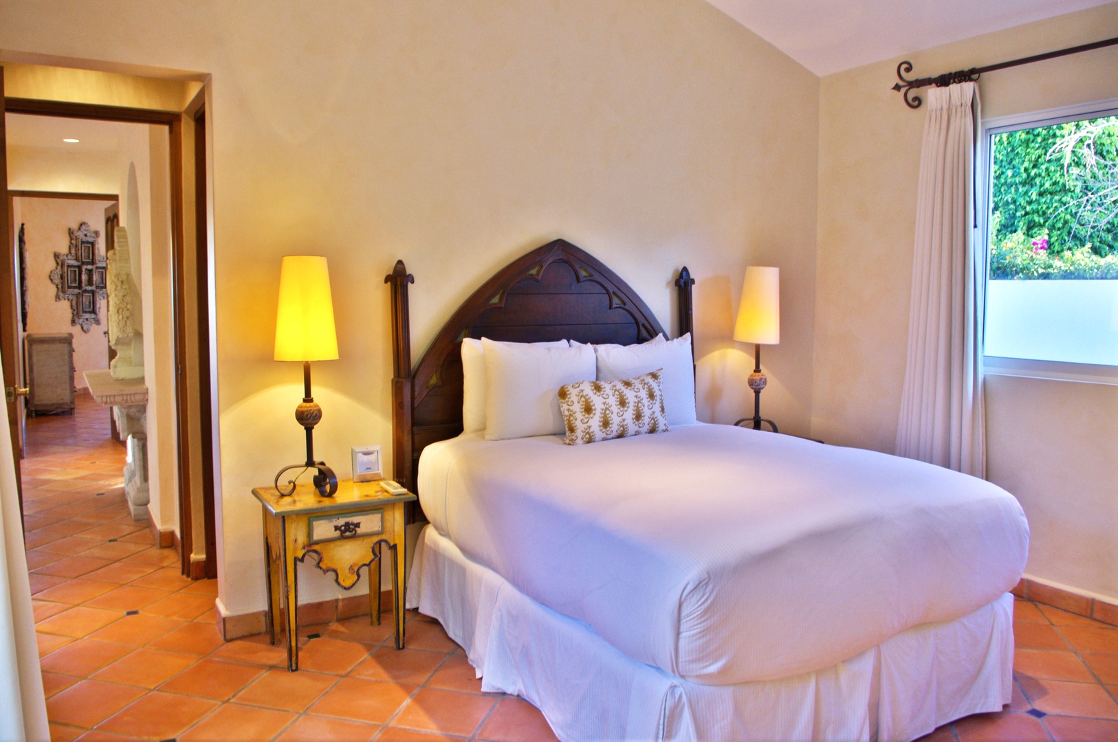 Step into your serene retreat with a plush bed draped in crisp linens, warm lamps casting a gentle glow, and a peaceful garden view just beyond your window.