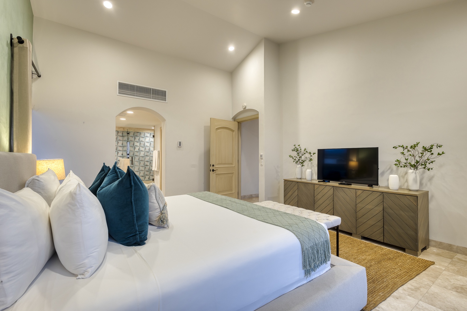 Sink into soft white linens and plush navy pillows after a long day. Your private bedroom features a flat-screen TV, stylish wood furnishings, and serene archway details that invite instant relaxation.