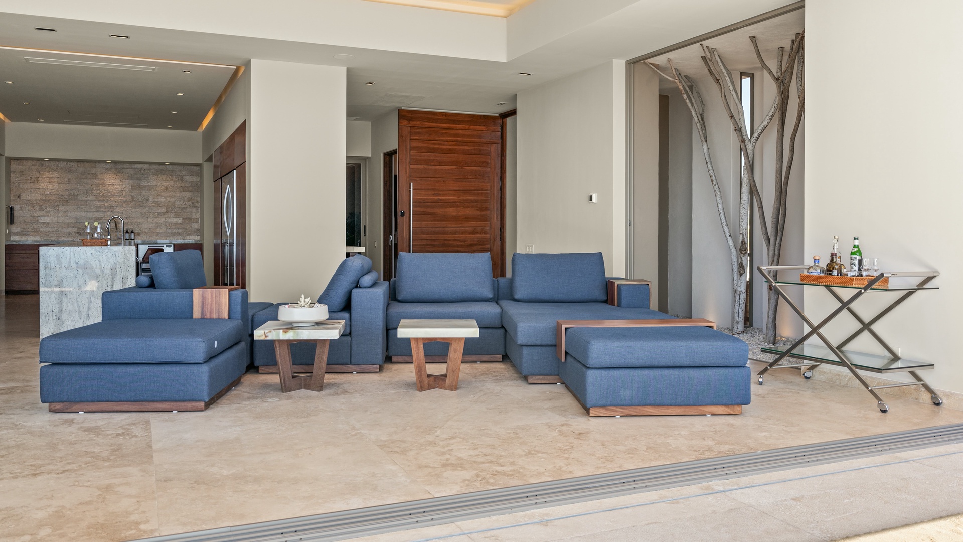 Sink into plush blue sofas and ottomans in your open-concept living space. Natural wood accents and a rustic branch sculpture add warmth, while the sleek kitchen awaits your culinary adventures just steps away.