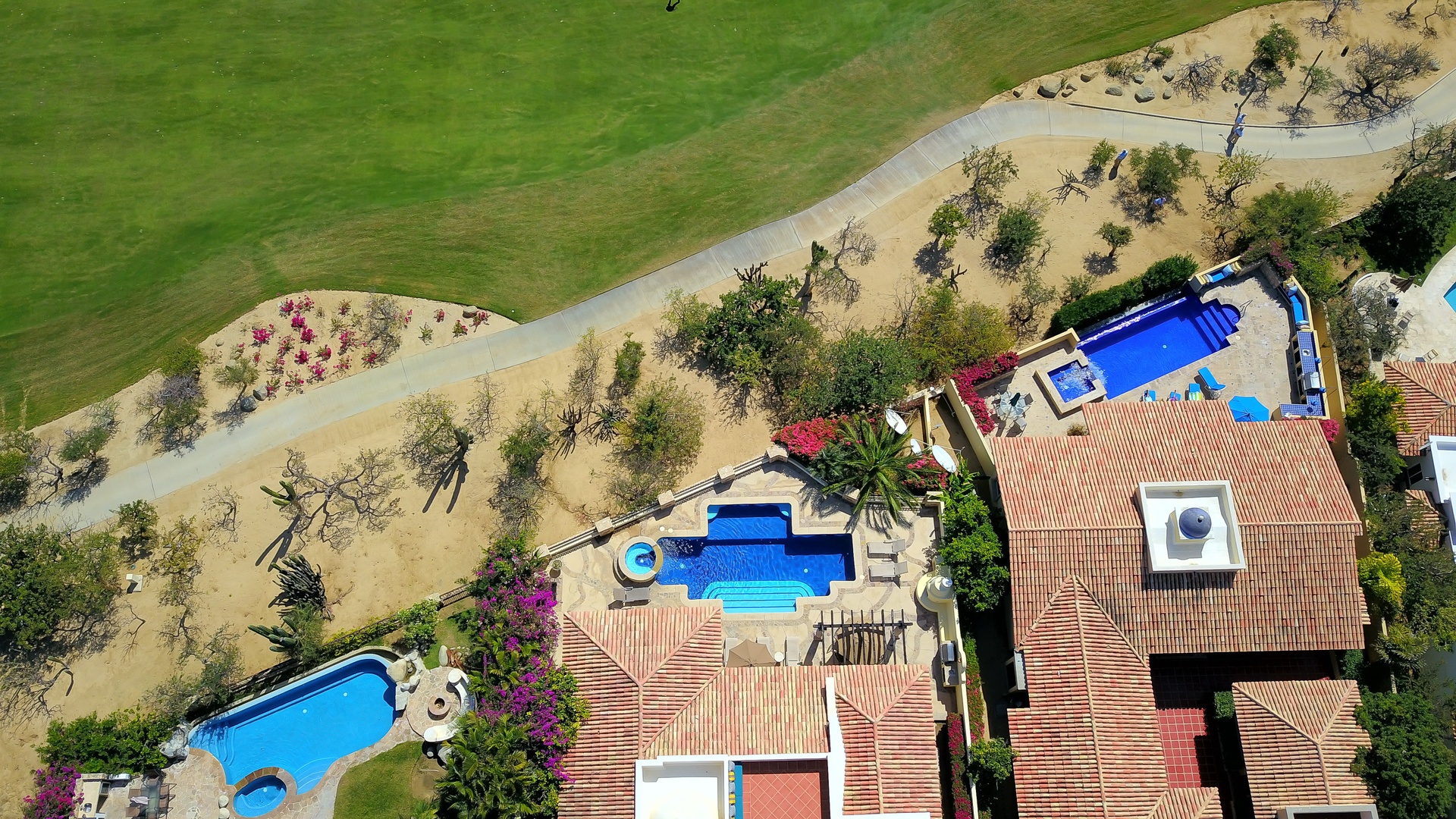 Aerial view of vacation properties featuring swimming pools and lush landscaping near open green spaces.