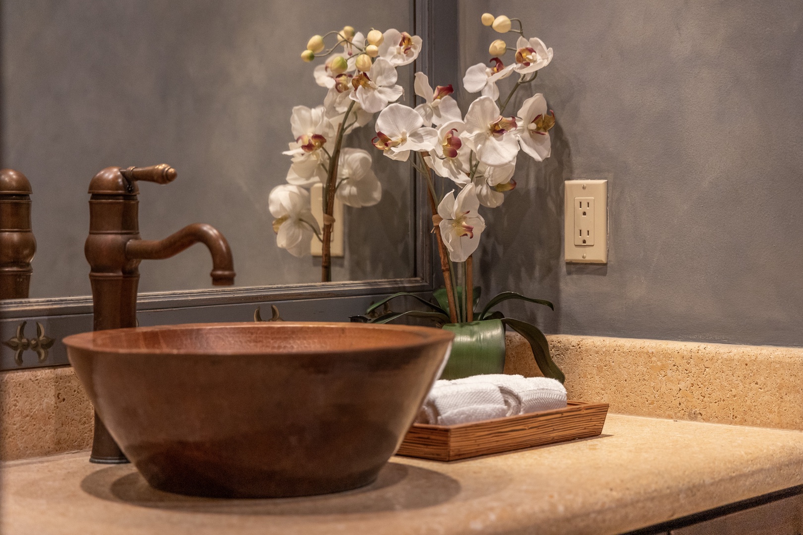 A copper vessel sink and warm-toned fixtures create a spa-like ambiance, while fresh orchids and soft towels invite you to unwind in style.