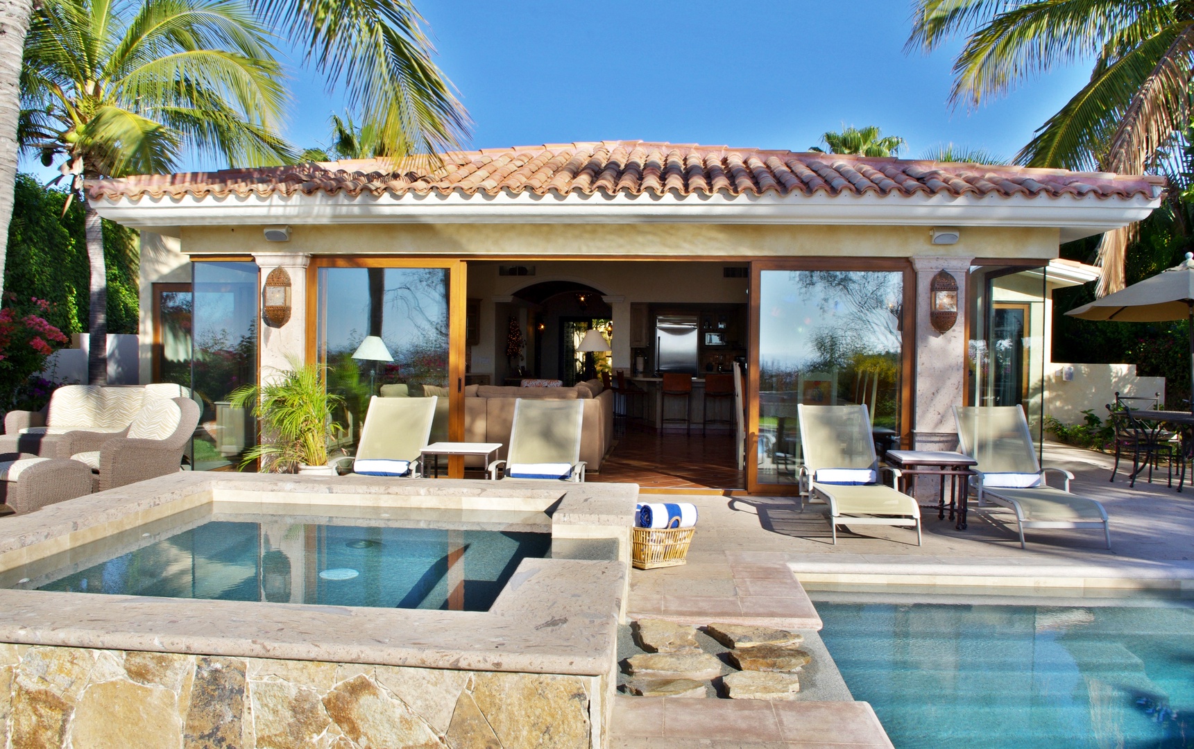 Property exterior showcasing a terracotta-tiled roof villa with an inviting pool area, framed by tropical palm trees under clear blue skies.