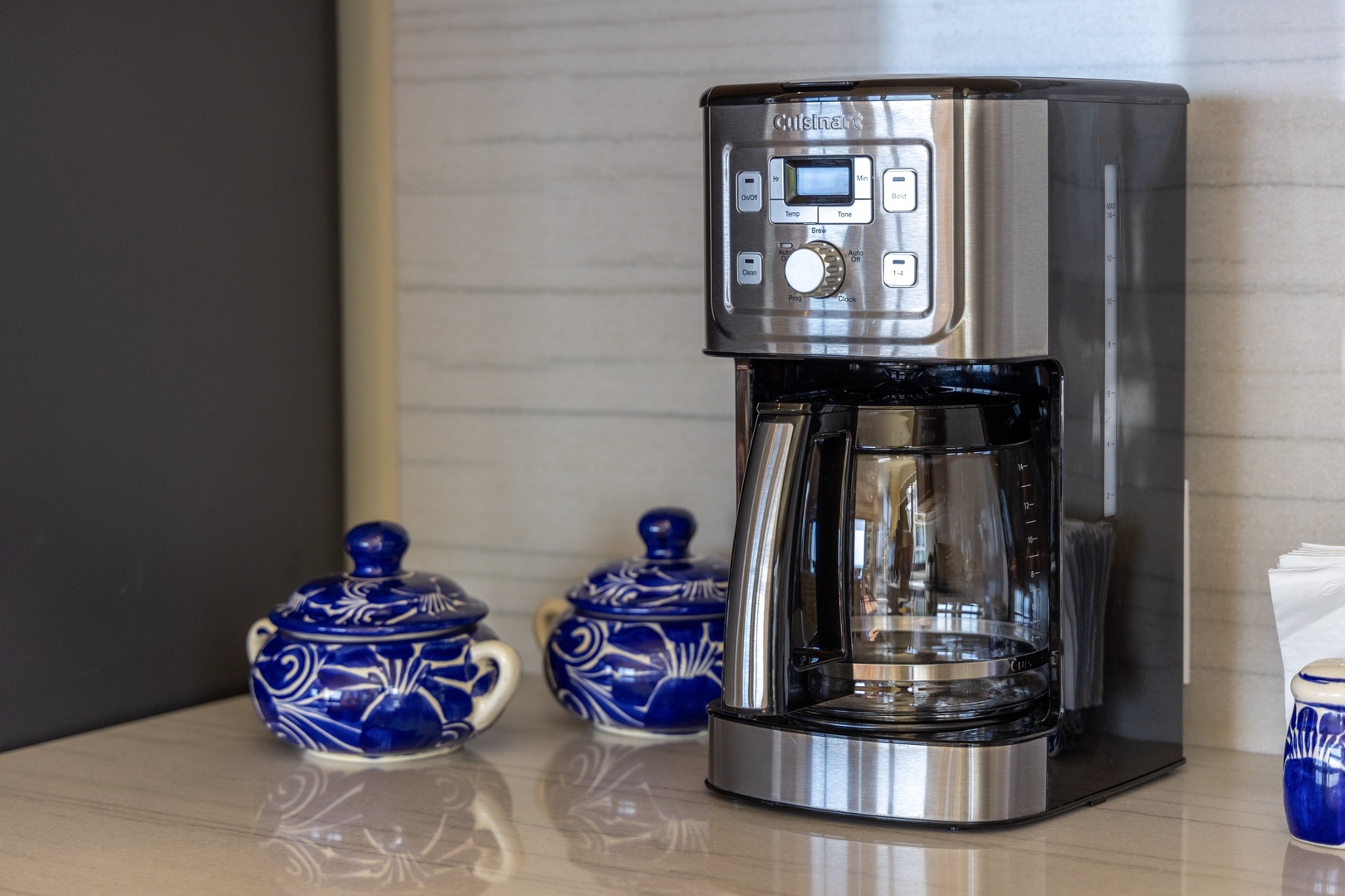 A sleek stainless steel coffee maker stands ready to brew your perfect morning cup, complemented by charming blue and white ceramic tea accessories for your preferred hot beverage.