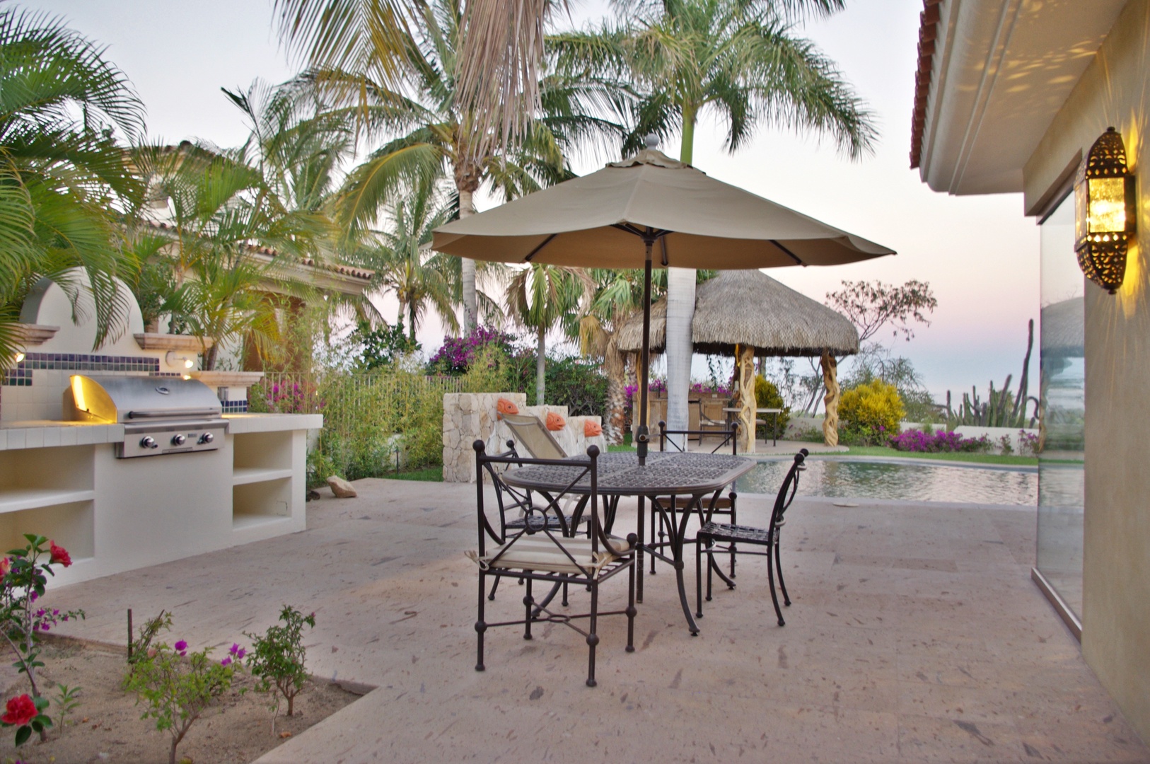 Expansive beachfront patio area featuring outdoor dining, BBQ facilities, and pool with tropical palms and ocean backdrop. Part of the property's exterior amenities and surrounding landscape.