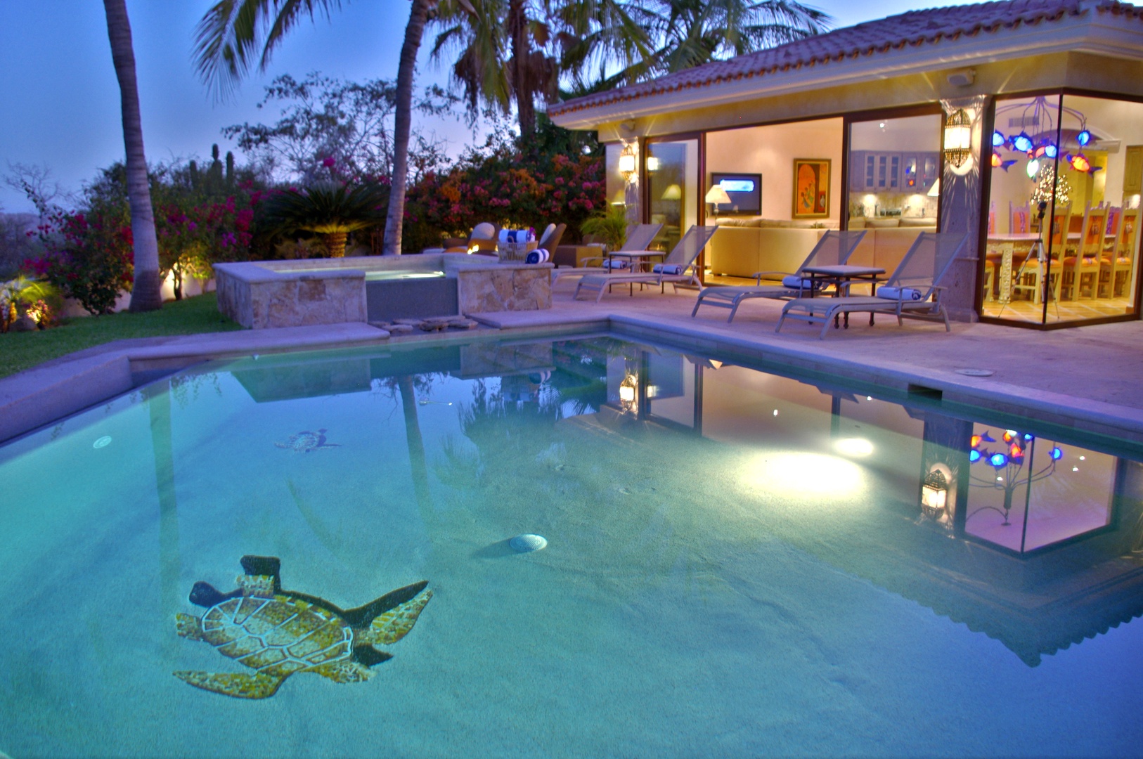 Twilight reveals a stunning mosaic sea turtle adorning your private pool, surrounded by lush palms and tropical gardens, with inviting loungers waiting just steps from elegant indoor spaces.