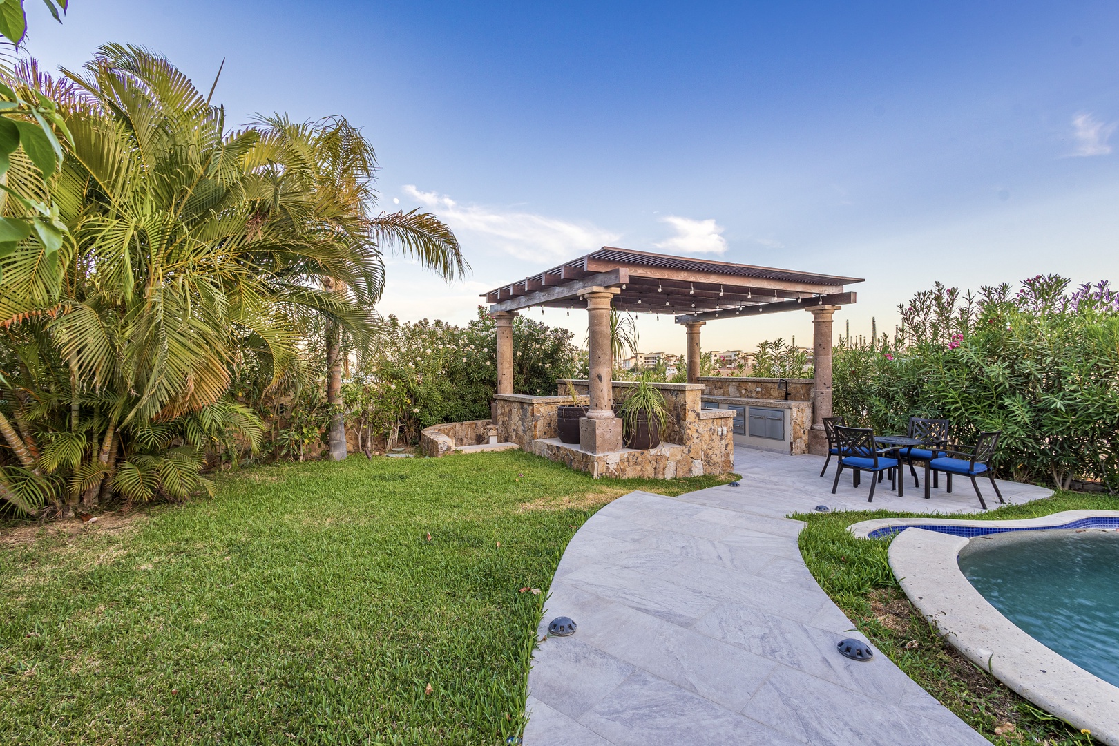 Lush tropical landscaping frames this inviting outdoor paradise, where manicured lawns lead to a shaded pergola and sparkling pool—your private retreat for unforgettable gatherings under the sun.