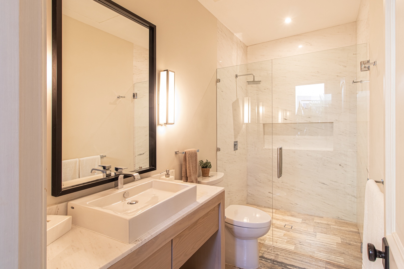 Refresh yourself in this bright modern bathroom with a spacious walk-in shower, elegant marble finishes, and thoughtful touches like soft towels and warm lighting.