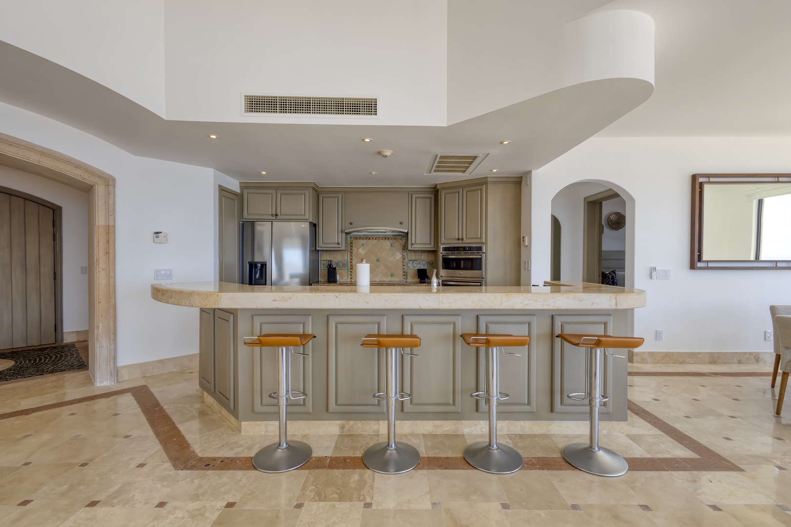 Picture yourself preparing meals at this spacious kitchen island, where elegant stone countertops and modern appliances meet distinctive architectural curves overhead, creating your perfect vacation cooking space.