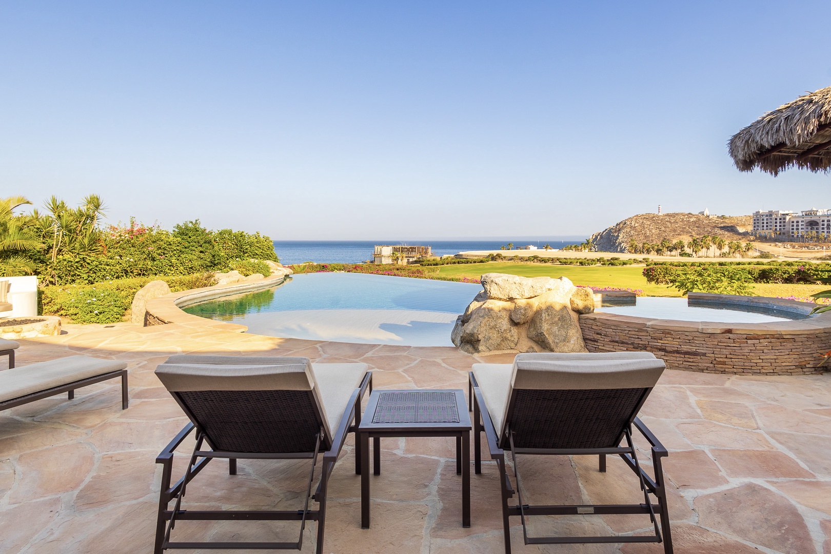 Coastal resort property featuring infinity pool and ocean views across a golf course landscape with nearby hillside development.