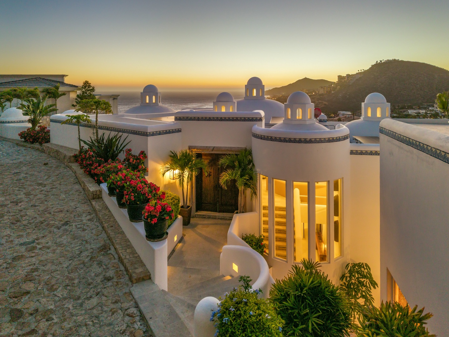 Stunning Mediterranean architecture glows against dramatic sunset backdrop, showcasing unique domed structures and hillside location.