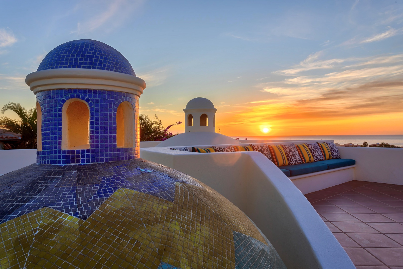 Stunning rooftop terrace featuring colorful mosaic domes and built-in seating with ocean sunset views stretching to the horizon.