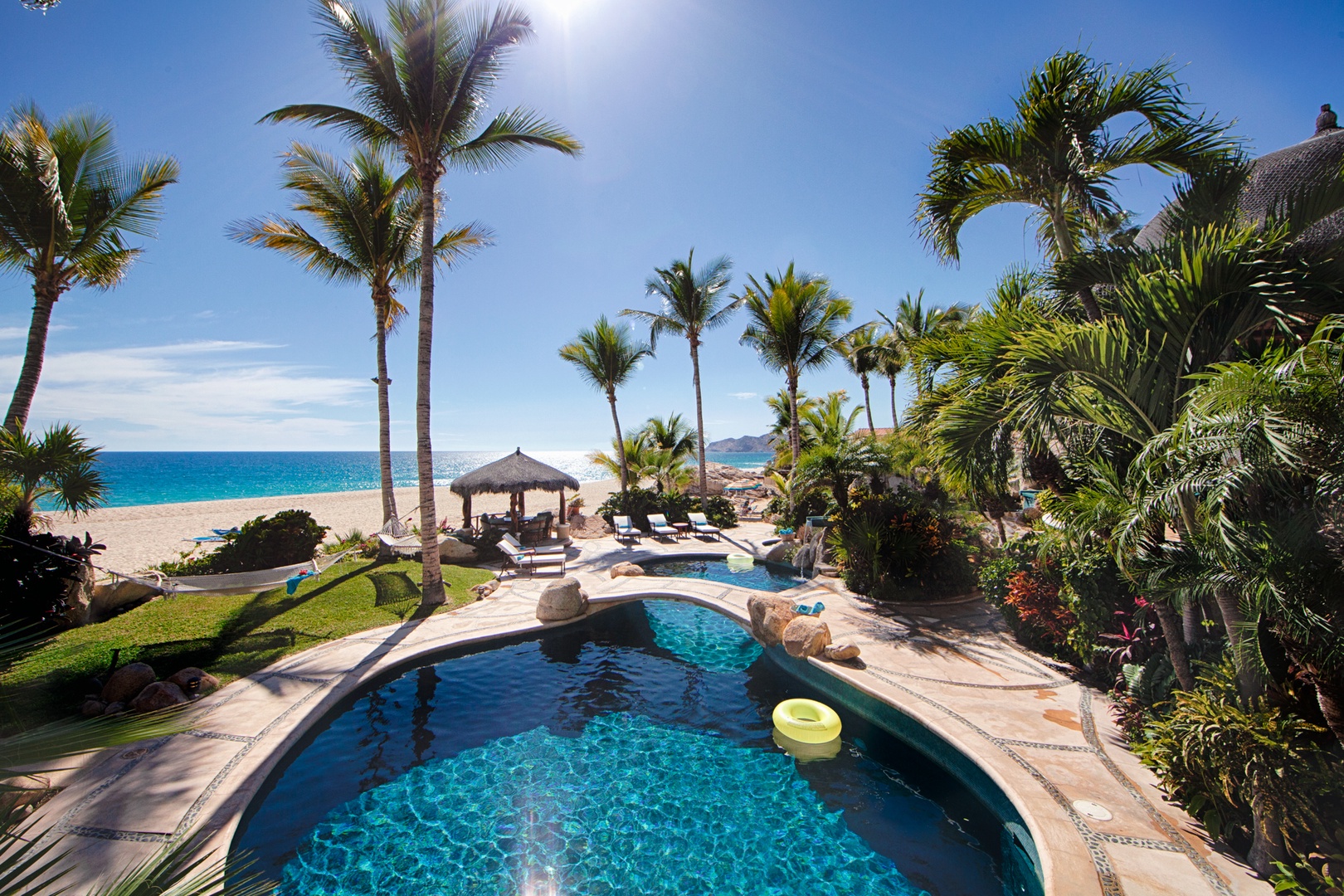 Tropical paradise with private pool, palm trees, and direct beach access beneath brilliant blue skies.