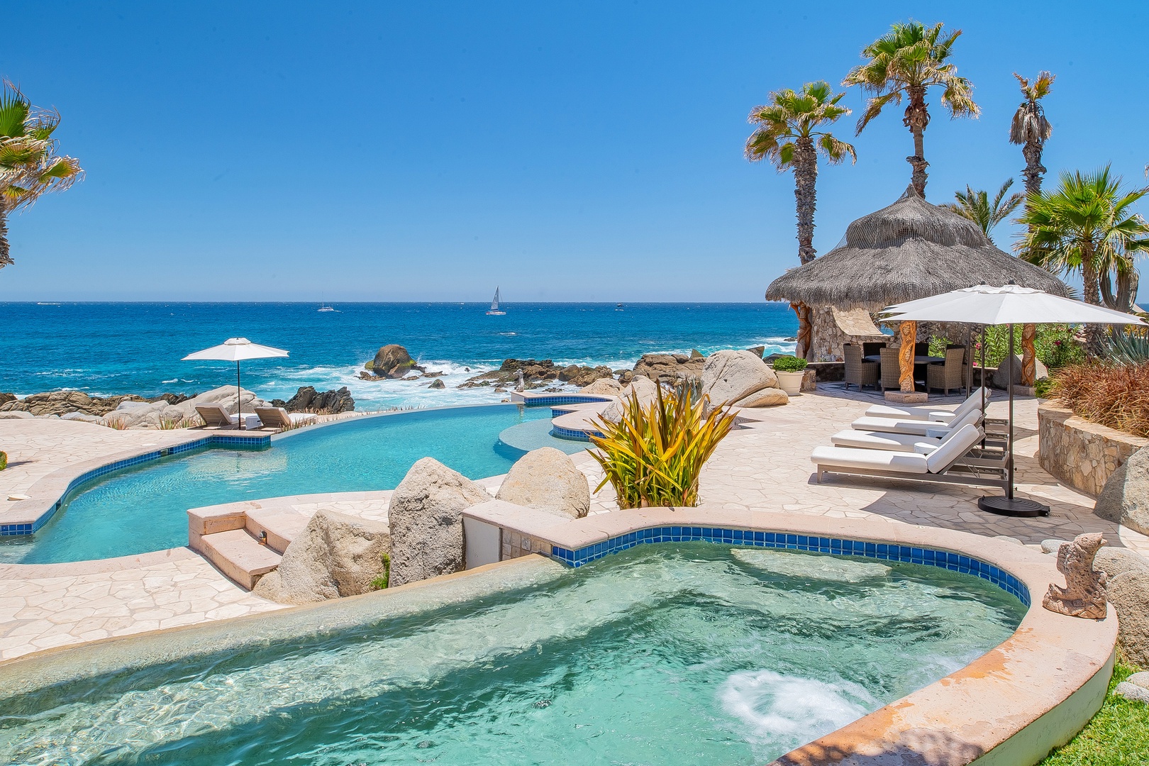 Tropical paradise with infinity pool and hot tub overlooking pristine ocean waters, surrounded by swaying palms.